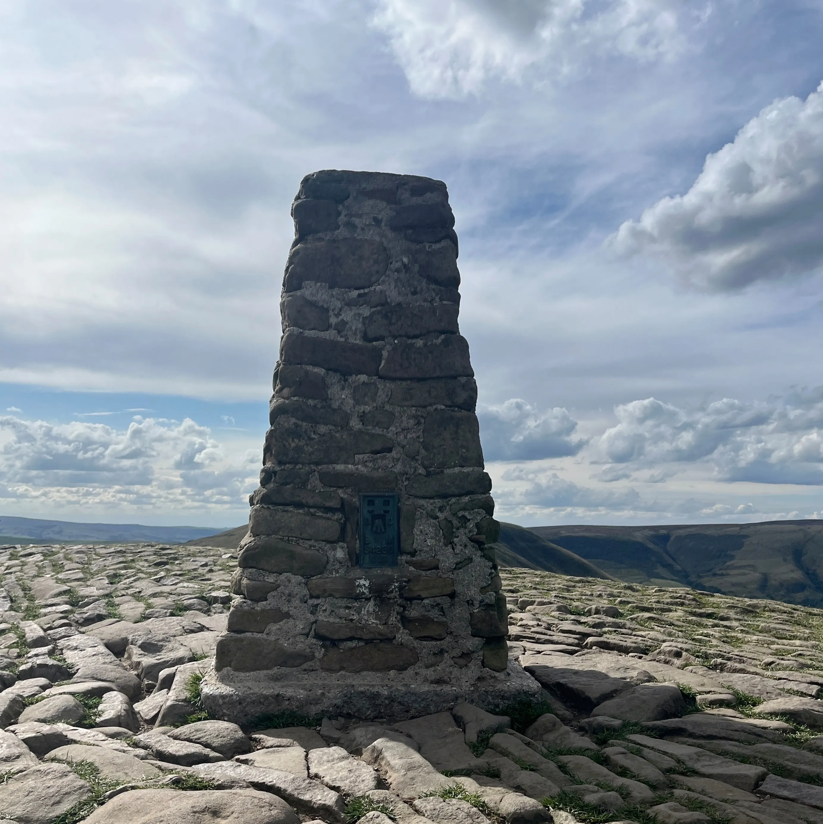 A stone brick square based pyramid with the top cut off flat. A plaque is embeded into the brick describing the location of Mam Tor