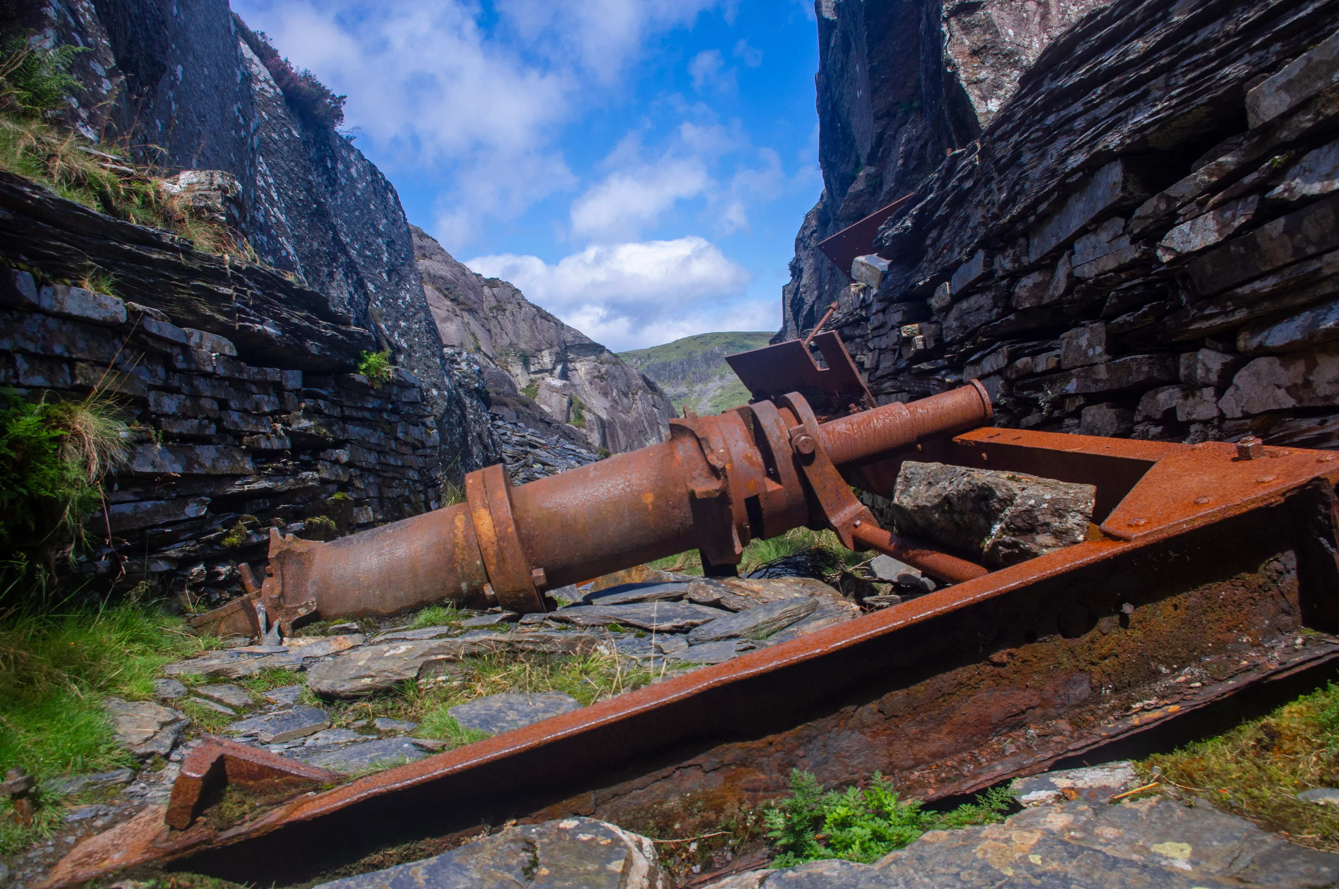 A photograph of rusted mine equipment with slate walls on either side
