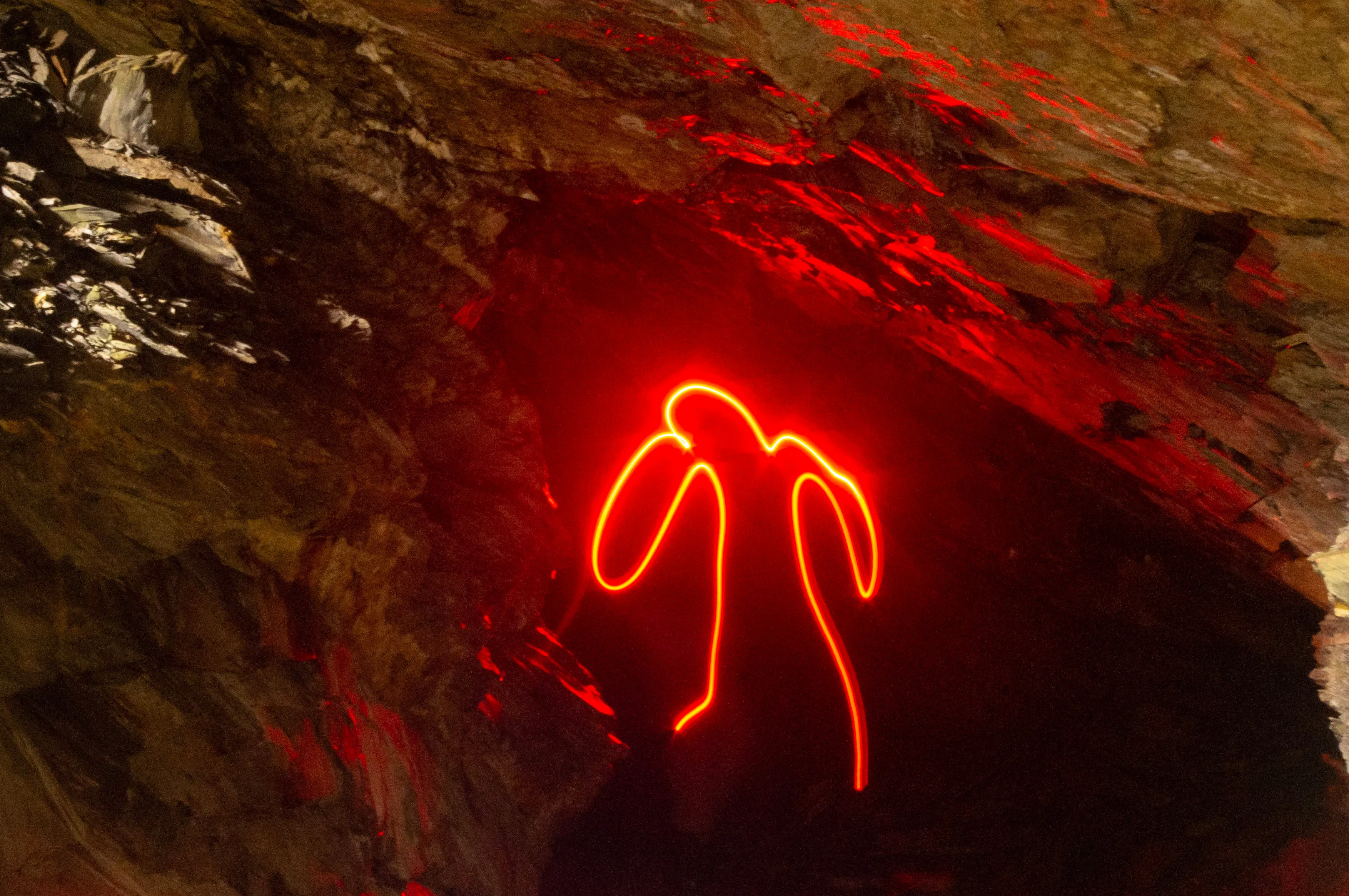 A photo of florecent man drawn with red light surrounded by rock