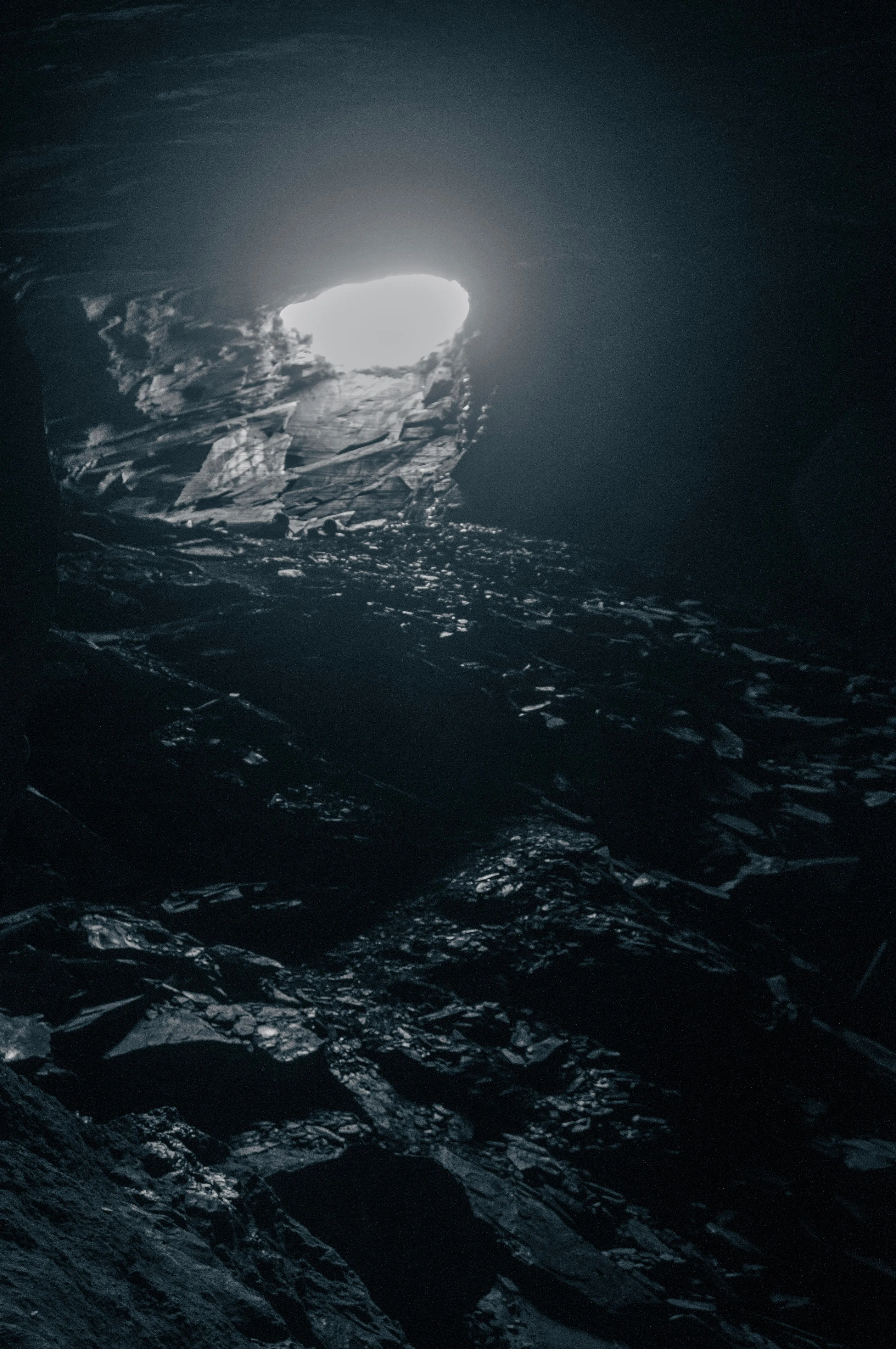 A photo of a tunnel entrance from inside a tunnel, with slate all over the floor.