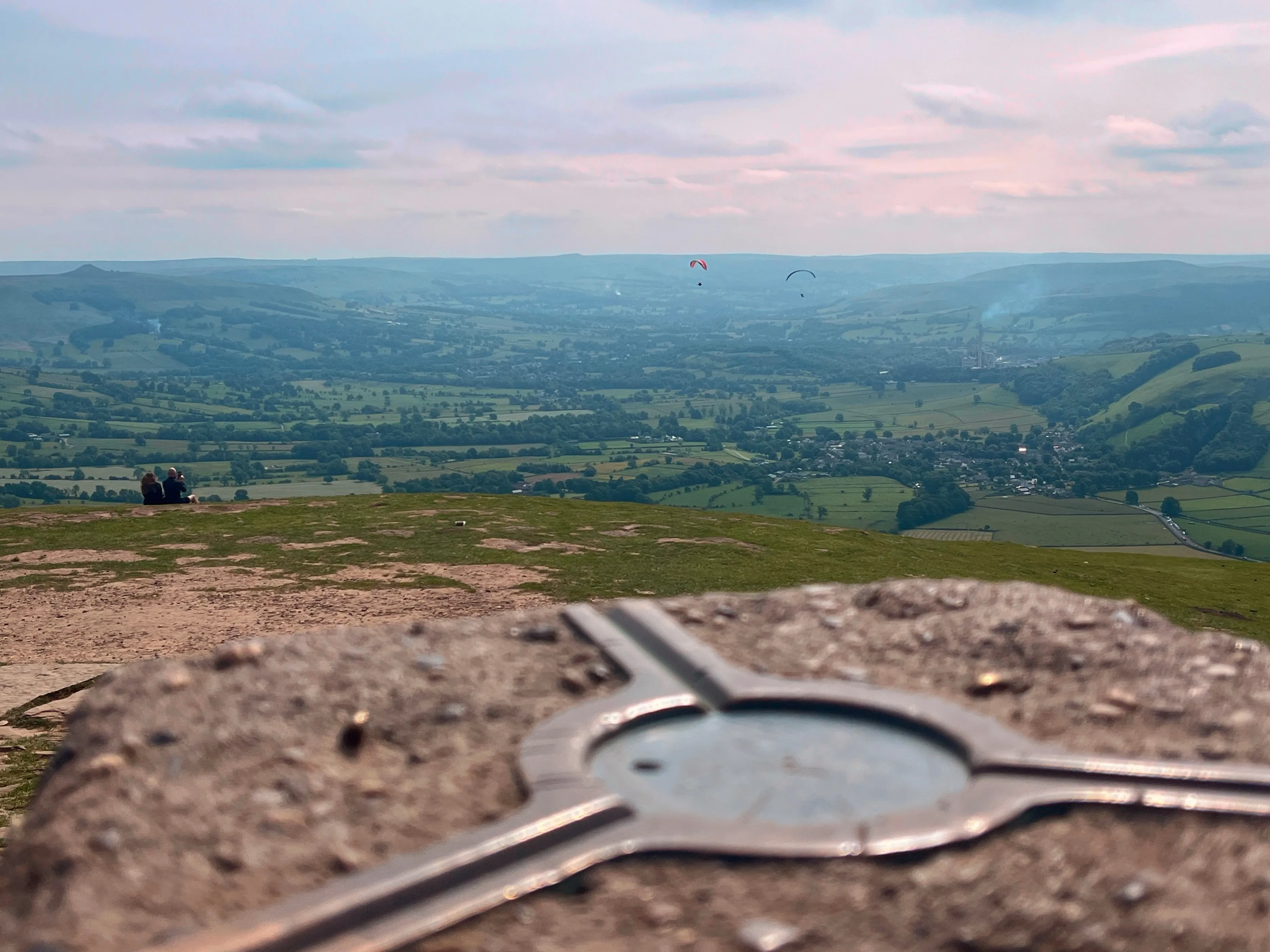Trig point at the top of Mam Tor with paragliders in the background